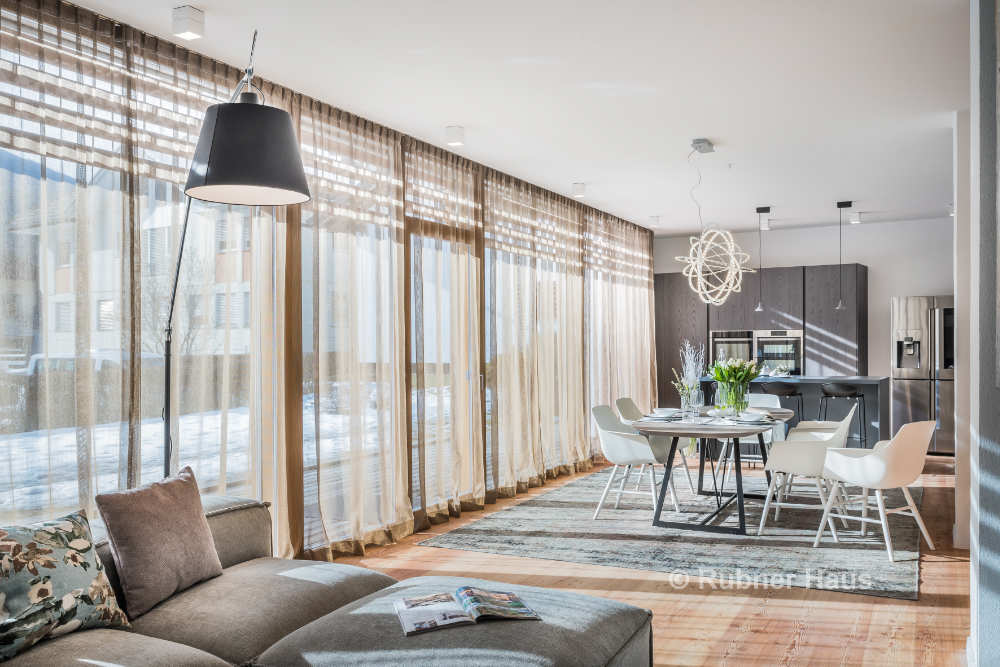 modern living room with gray couch, large windows, dining area, and lamps