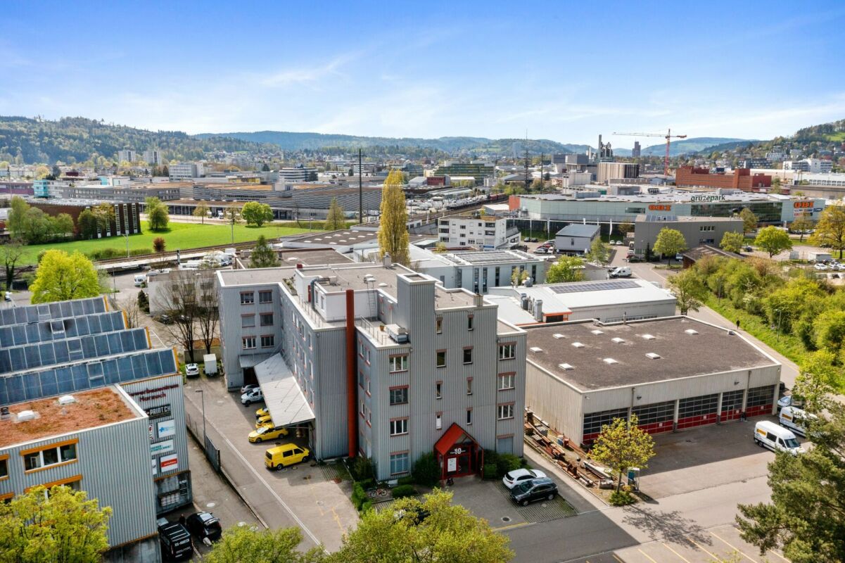Industrial building with multiple floors, solar panels on the roof, multiple cars parked, large parking area