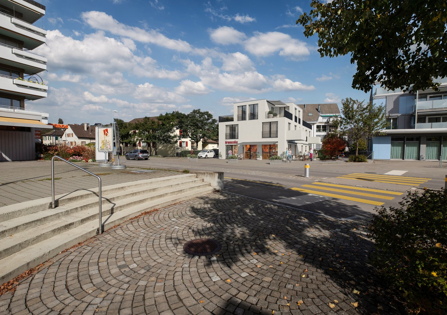 Modern building with large windows, parking area, concrete steps, brick pavement, street with cars, and sidewalk.