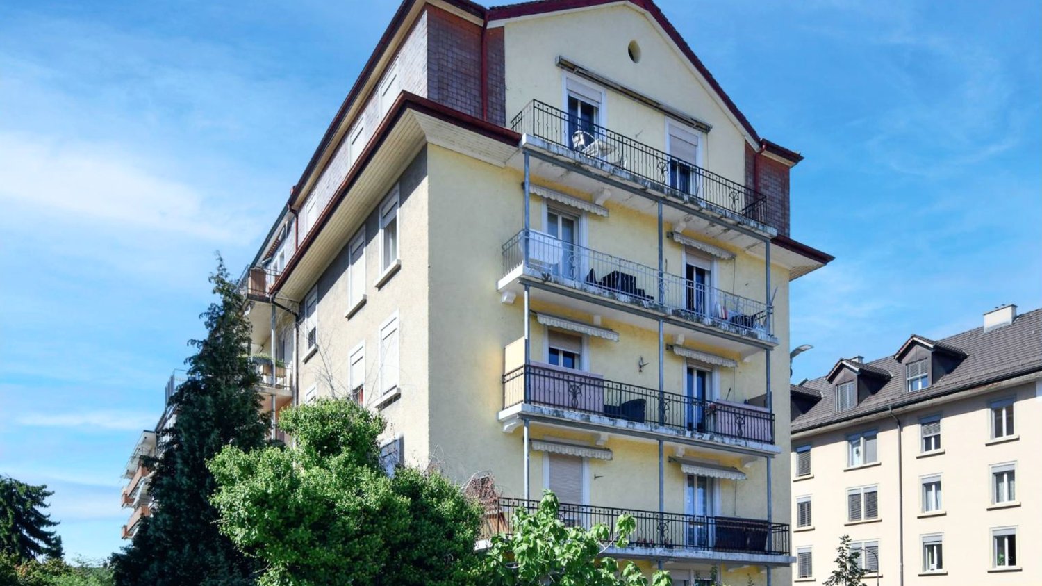 multi-story building with balconies, yellow exterior, several windows, trees in front