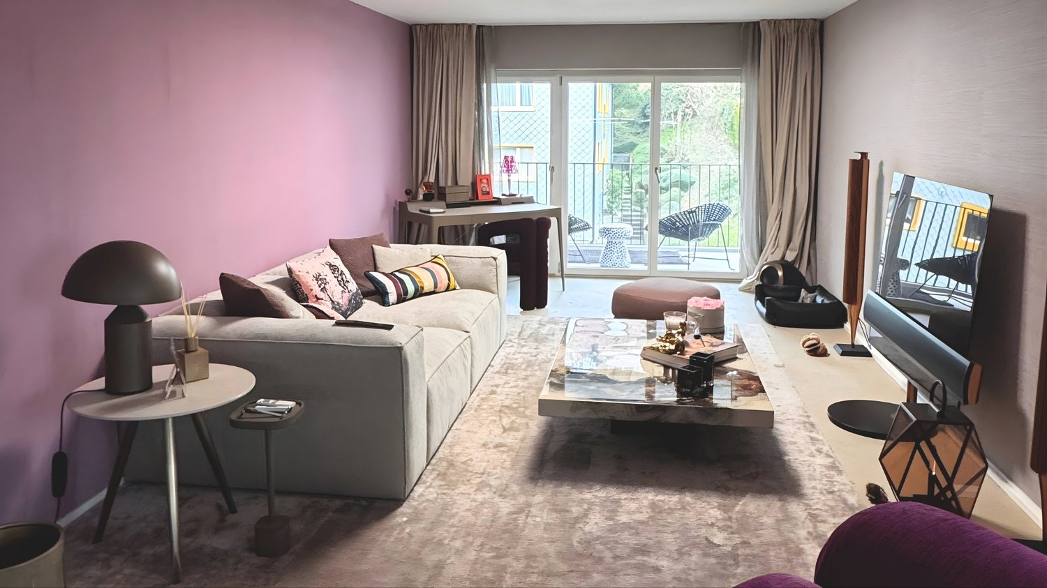 Contemporary design, pink walls, glass door to balcony, grey sofa, marble coffee table, desk with modern chairs, TV