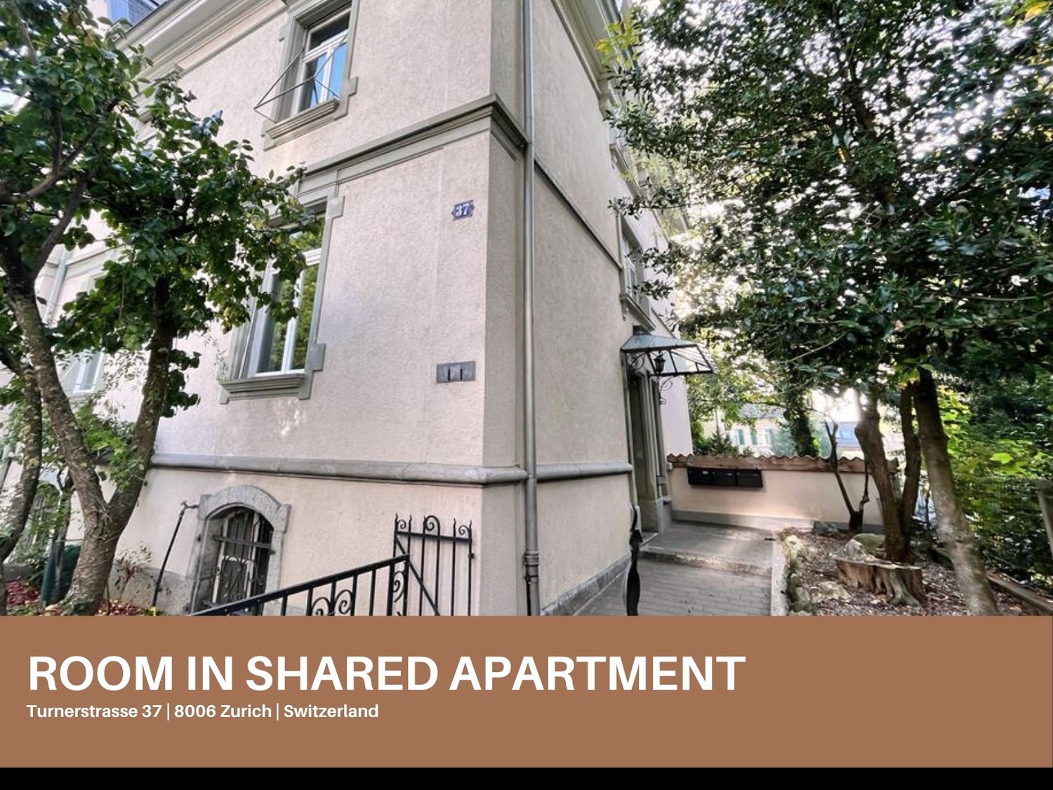 Exterior of an apartment building with cream-colored walls, glass windows, wrought iron gates and steps leading to the entrance.