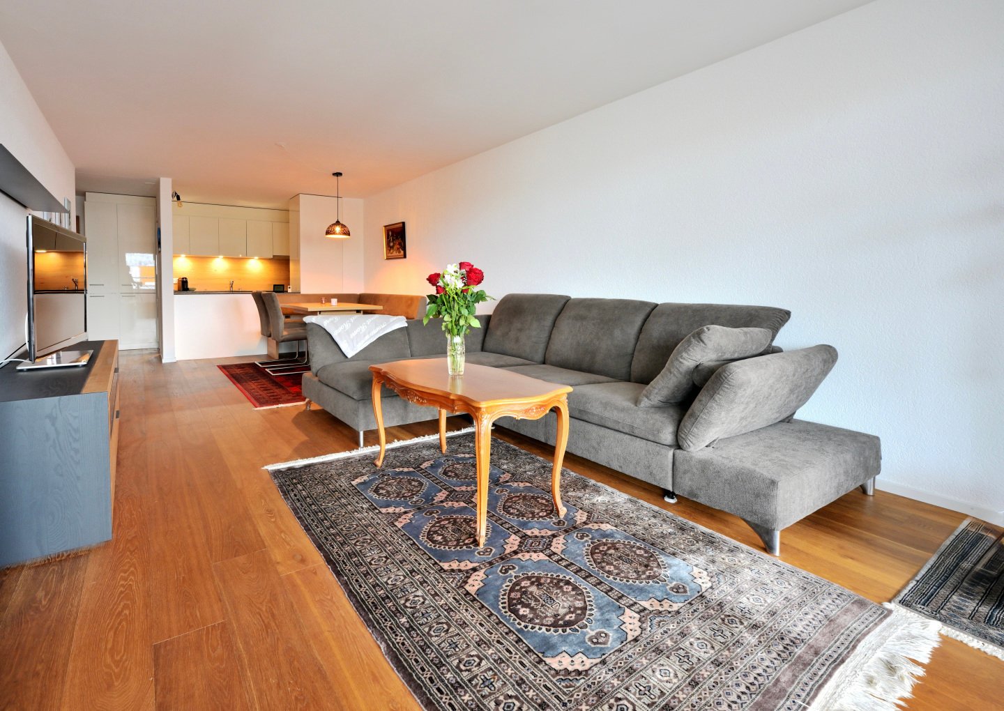 Cozy living area with a grey sofa, wooden coffee table, large rug, and a television