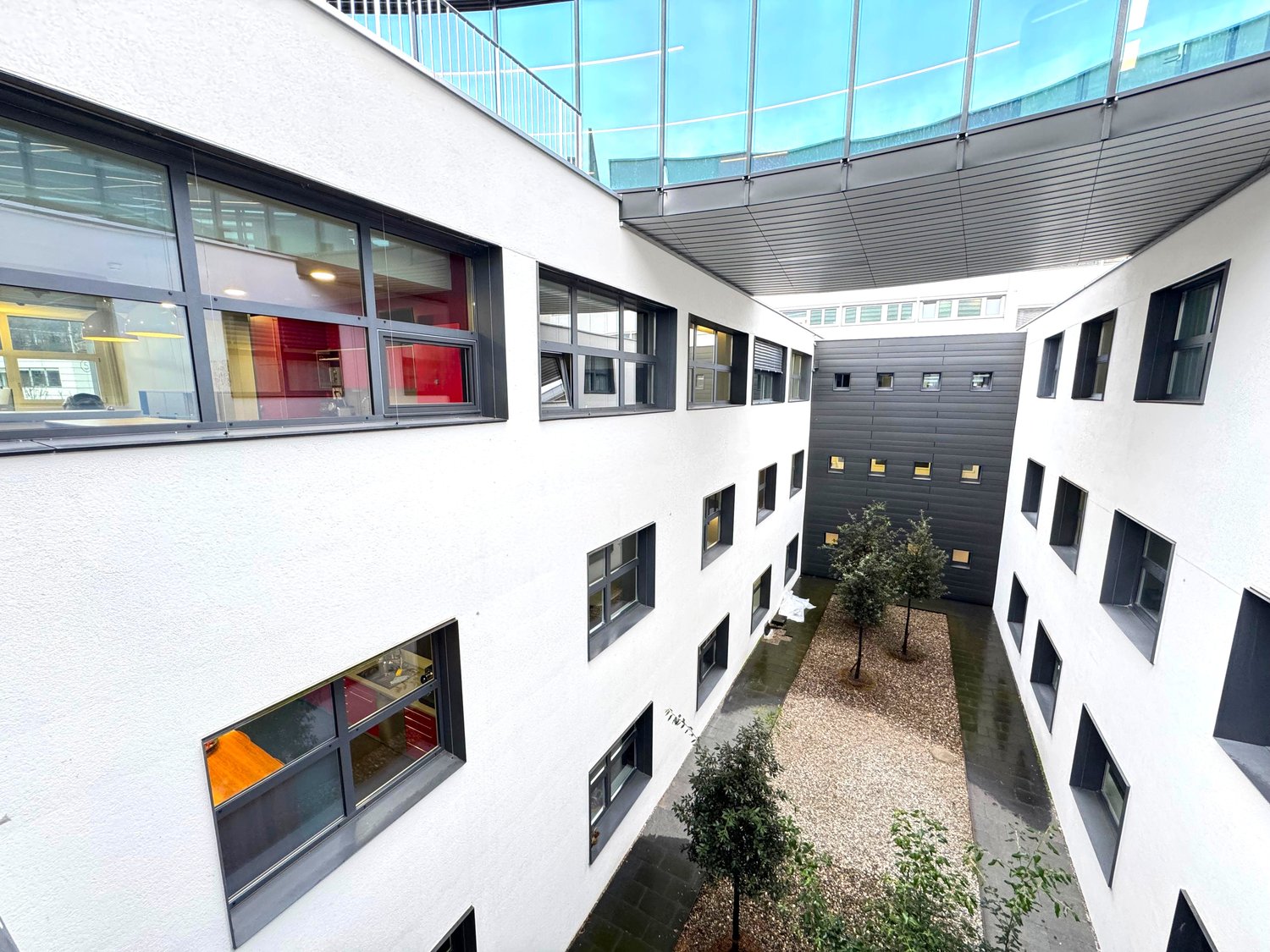 White exterior building, large windows, balcony on second floor, internal courtyard, small trees, tiled flooring