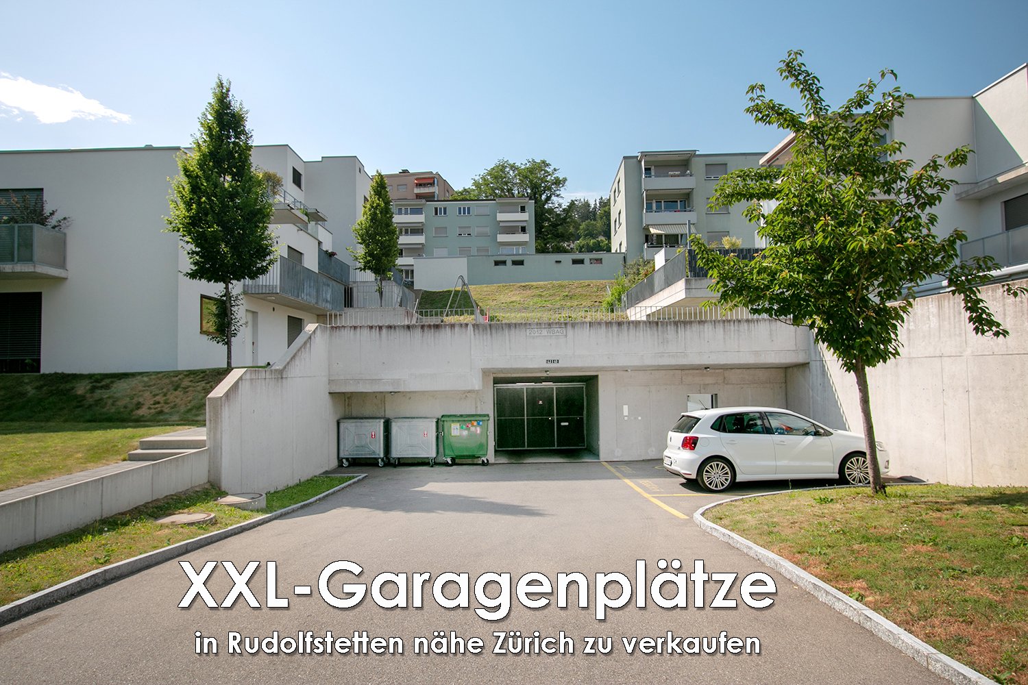 Multi-story apartment building with a garage and parking spaces located in Rudolfstetten near Zurich, Switzerland. The building has a modern, minimalist design with white and gray facades and trees surrounding the property.