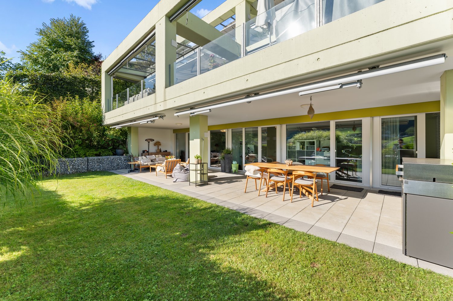 modern exterior with large windows, patio with dining table and chairs, balcony, and well-manicured lawn