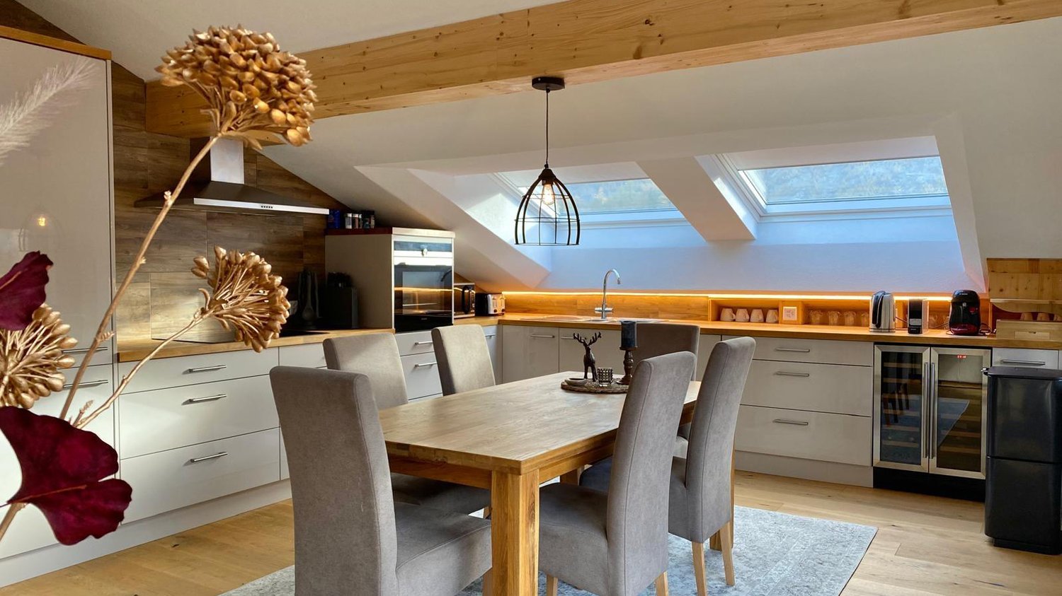 white kitchen, wooden floor, gray chairs, dining table, hanging lamp, kitchen appliances, two skylights