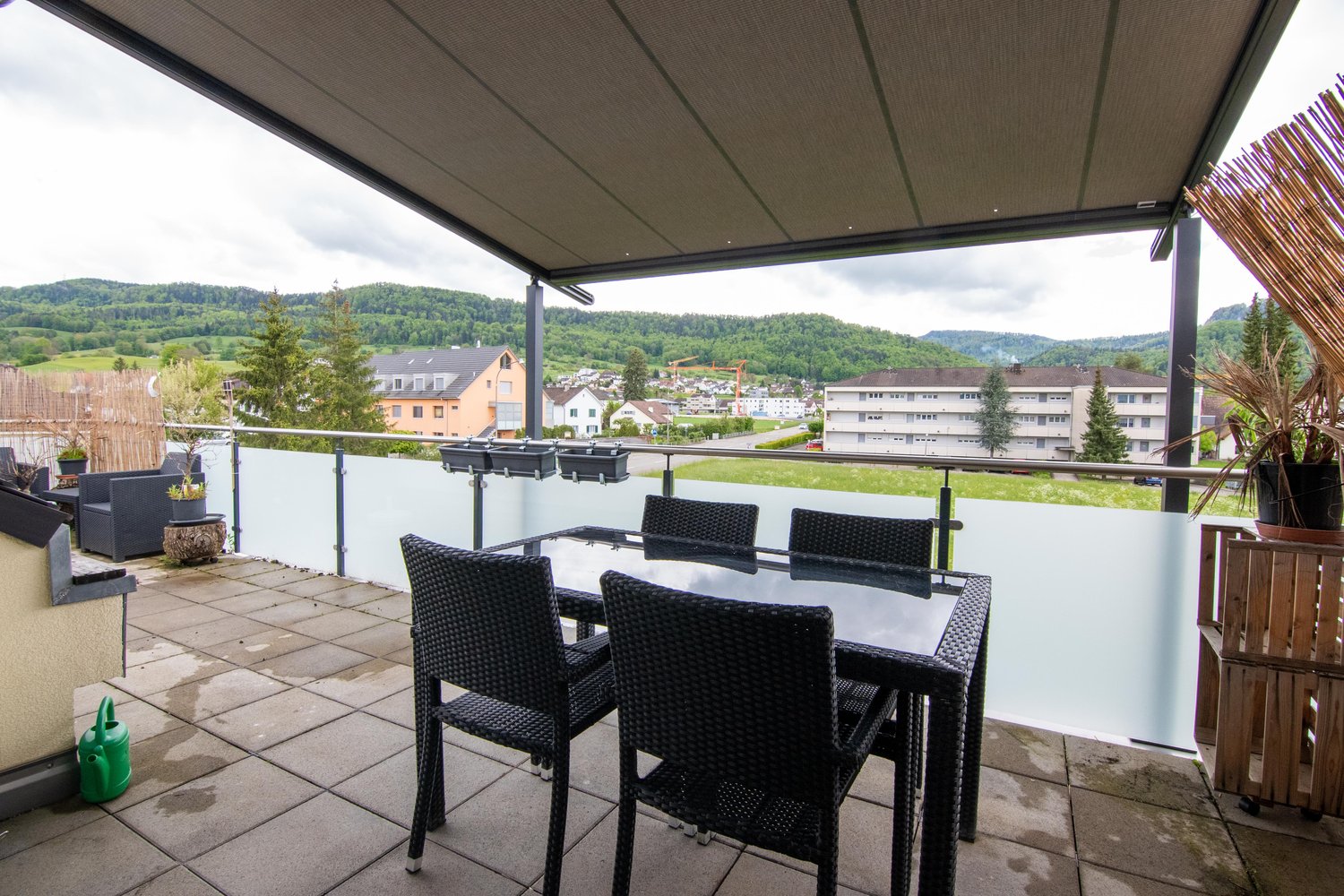 Covered balcony with black wicker furniture, overlooking a scenic mountain landscape with a town in the distance