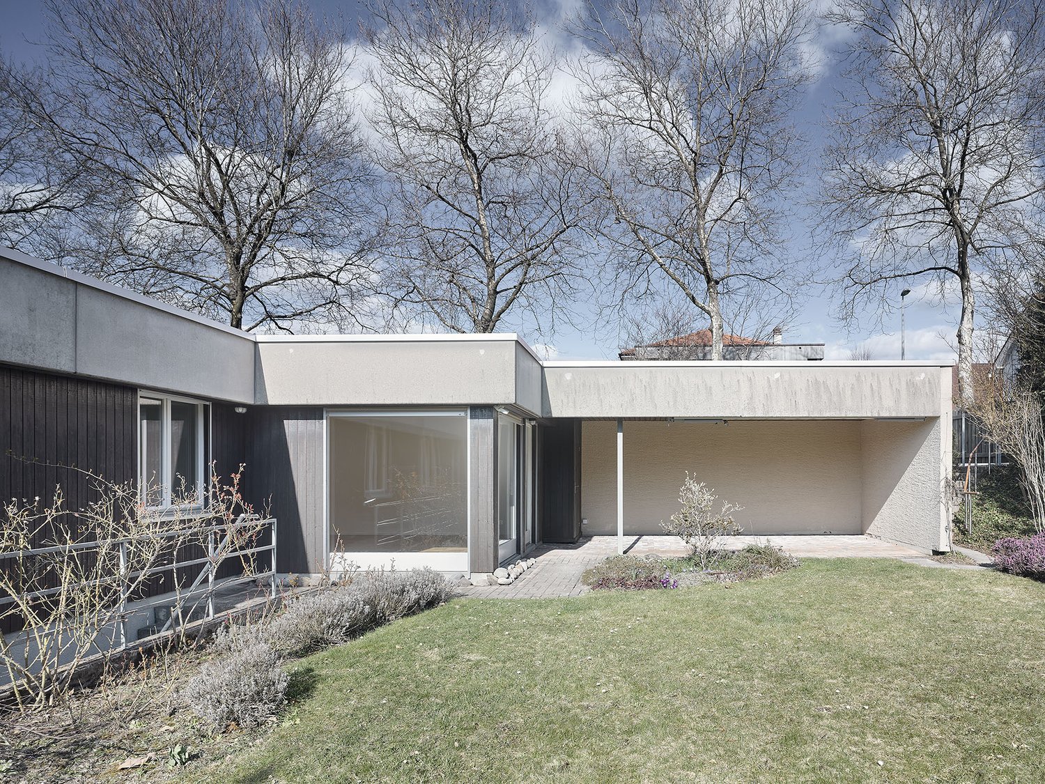 House exterior with two floors, large windows, well-manicured garden, concrete structure, trees in the background.