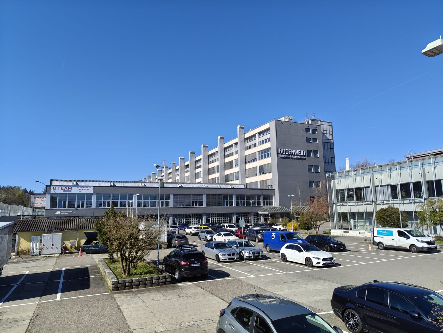 Large office building with multiple floors, surrounded by a parking lot with many cars parked.