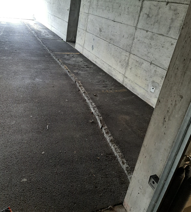 An empty concrete garage with a grey parking area and concrete walls. There is an access point with a white electrical socket