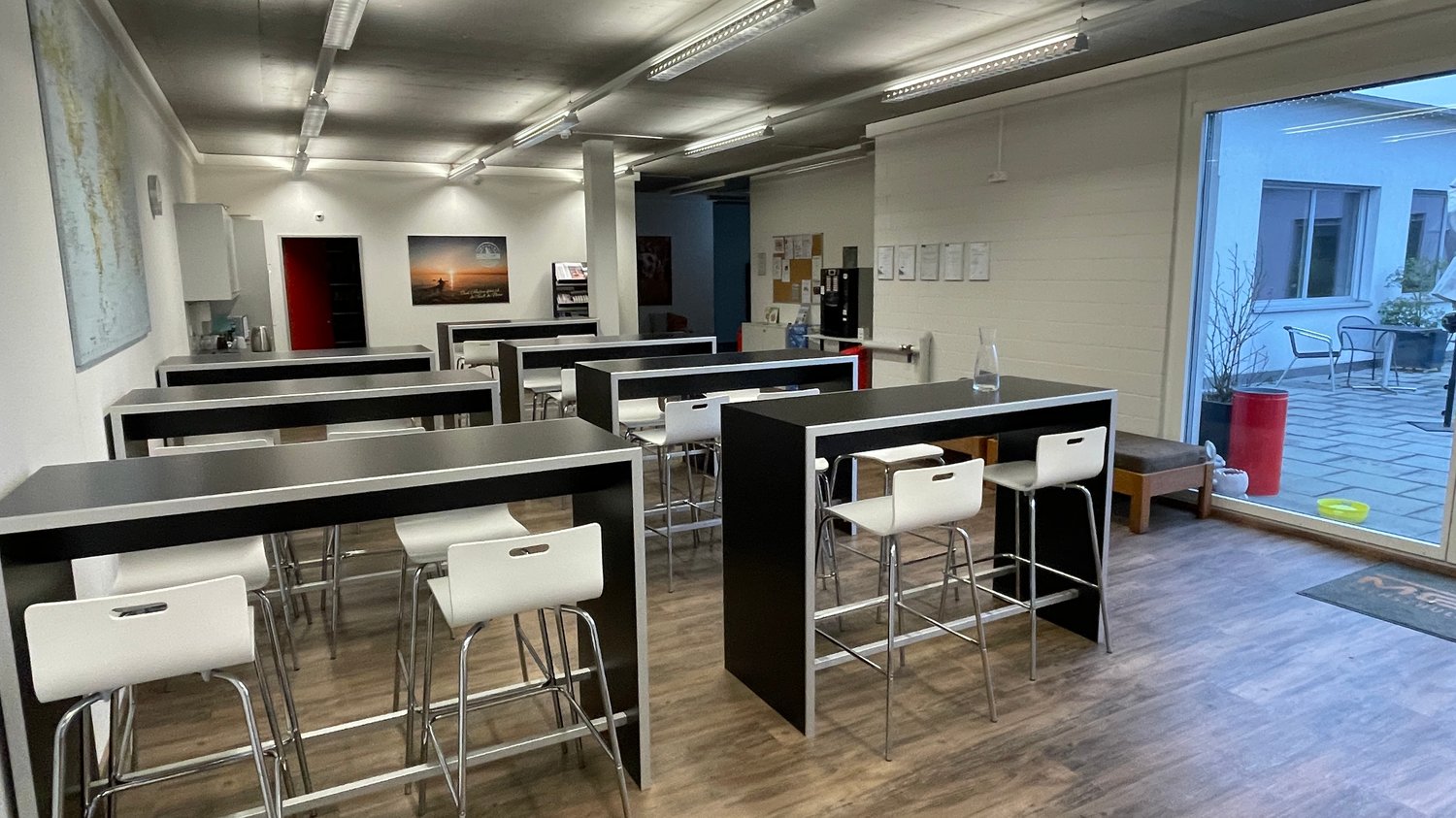 modern office room with black tables, white chairs, wooden floor, glass door, white walls, ceiling lights