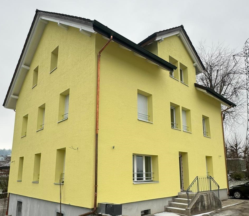 3-story yellow apartment building with white windows, balconies, and a copper downspout.