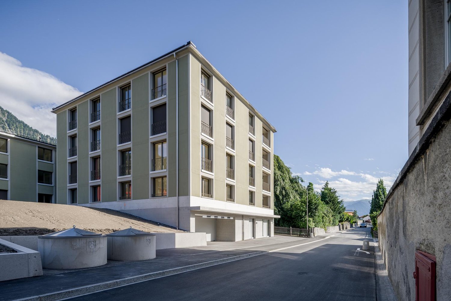 4-story apartment building with balconies, light-colored exterior, and parking spaces in front