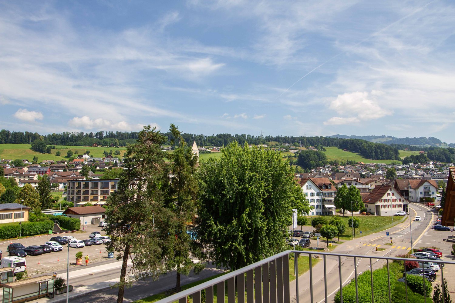 balcony with railings, view of the town with houses, green hills, cars parked