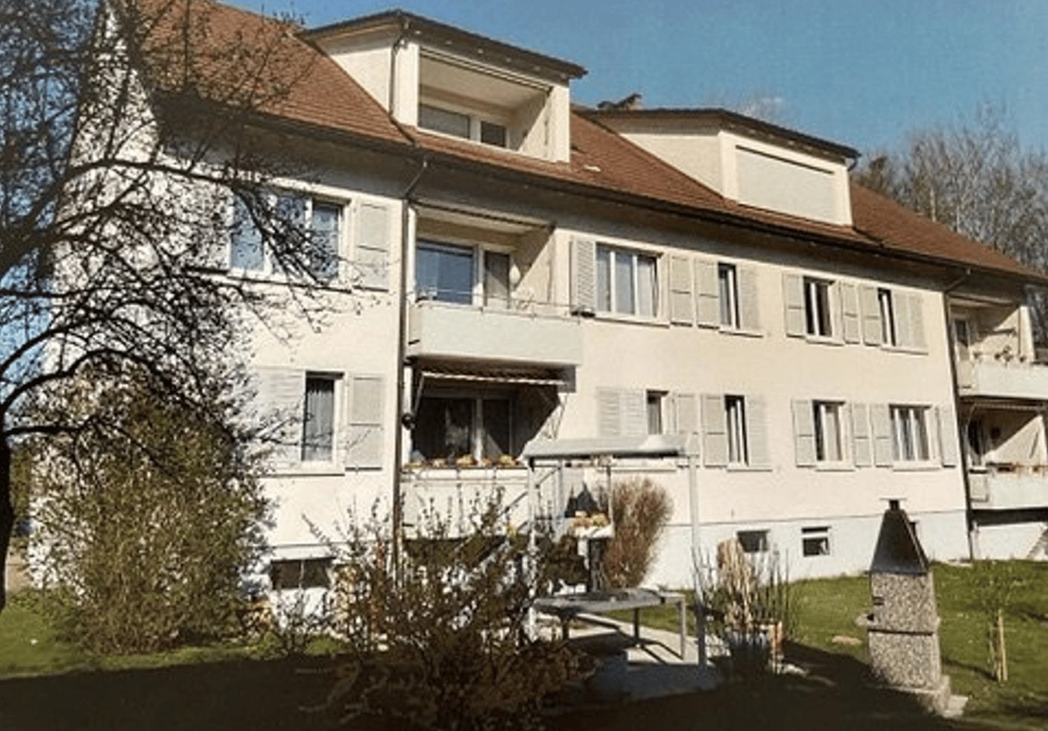 3-storey house, white paint, brown roof, balconies, trees, grass, small outdoor table