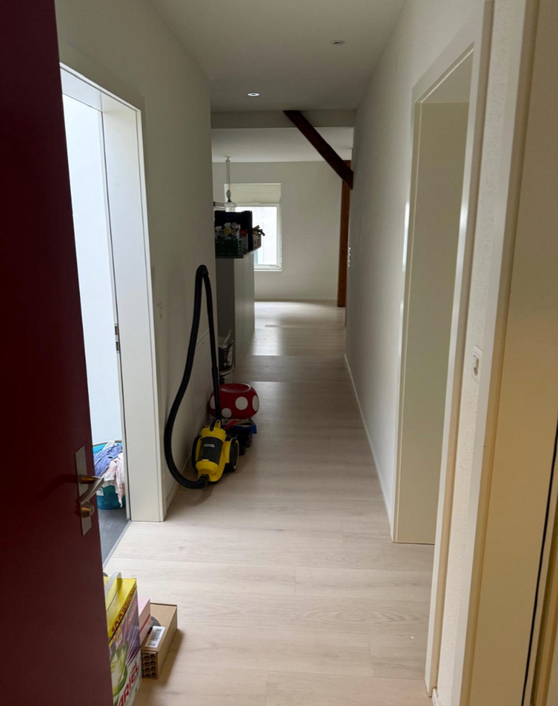 A hallway with wooden floors and white walls, a vacuum cleaner and a red mushroom toy lying on the floor.