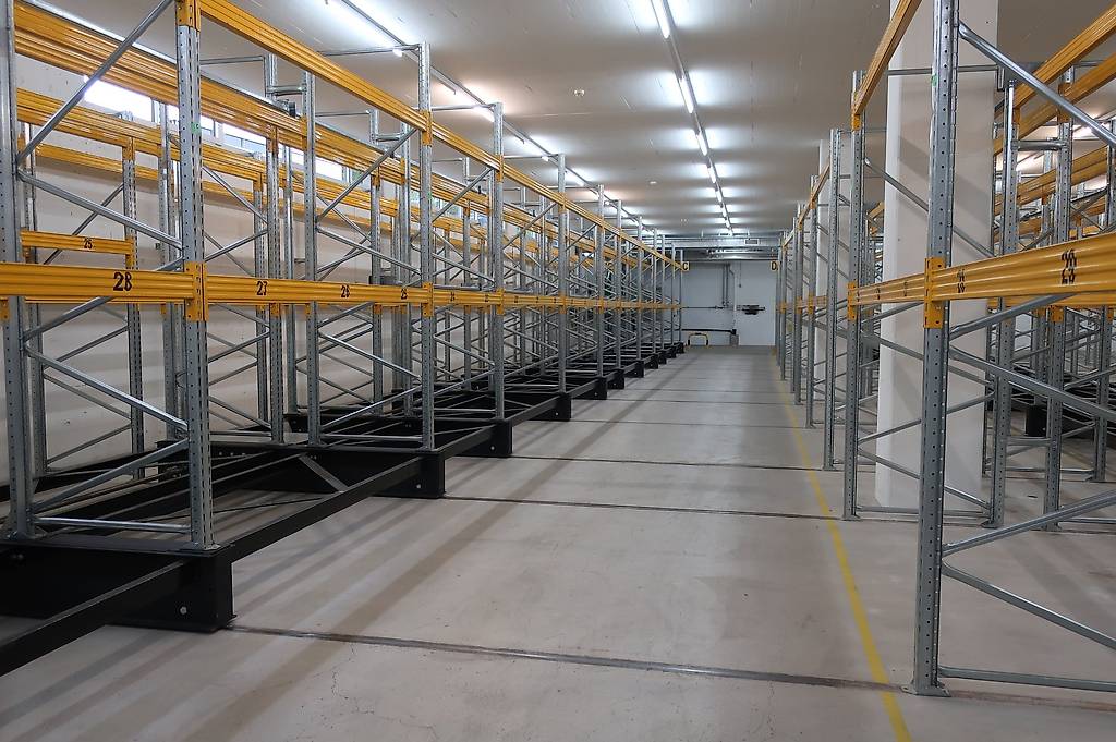Rows of pallet racking system, numbered shelves, yellow and silver construction, fluorescent ceiling lights, clean and spacious with yellow lines on the floor