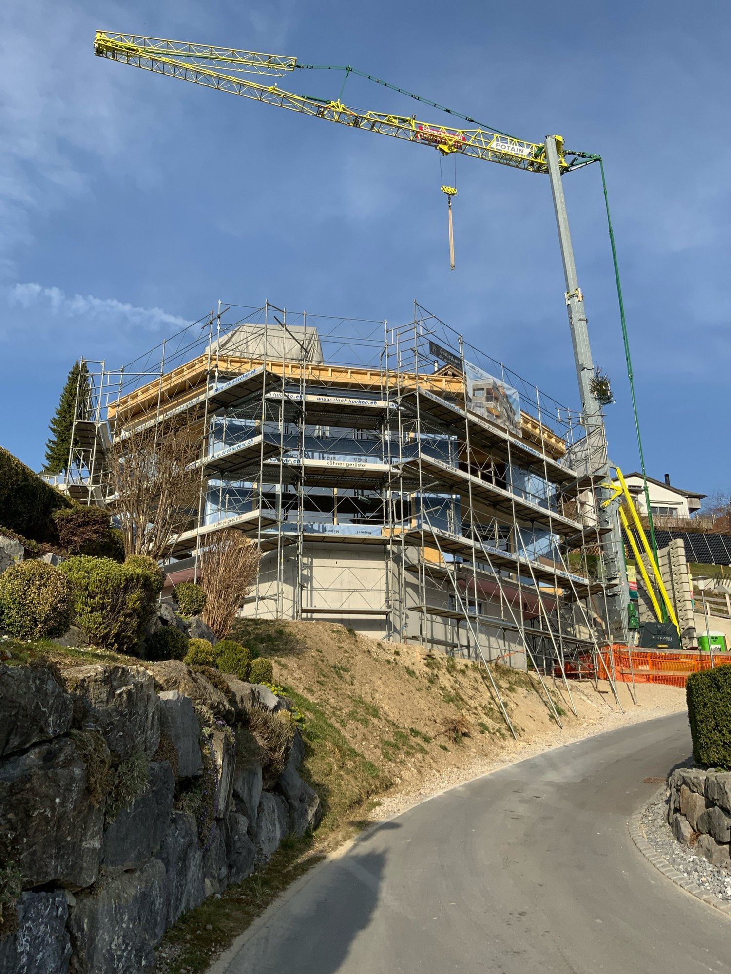 Building under construction, multiple floors, scaffolding, crane, road, rocks, plants