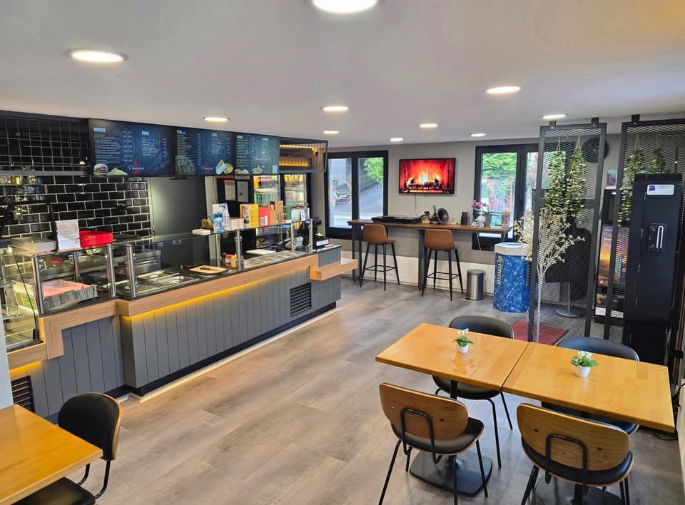 A modern restaurant with a wooden counter, black chairs, wooden tables, a fireplace, and a glass display case.