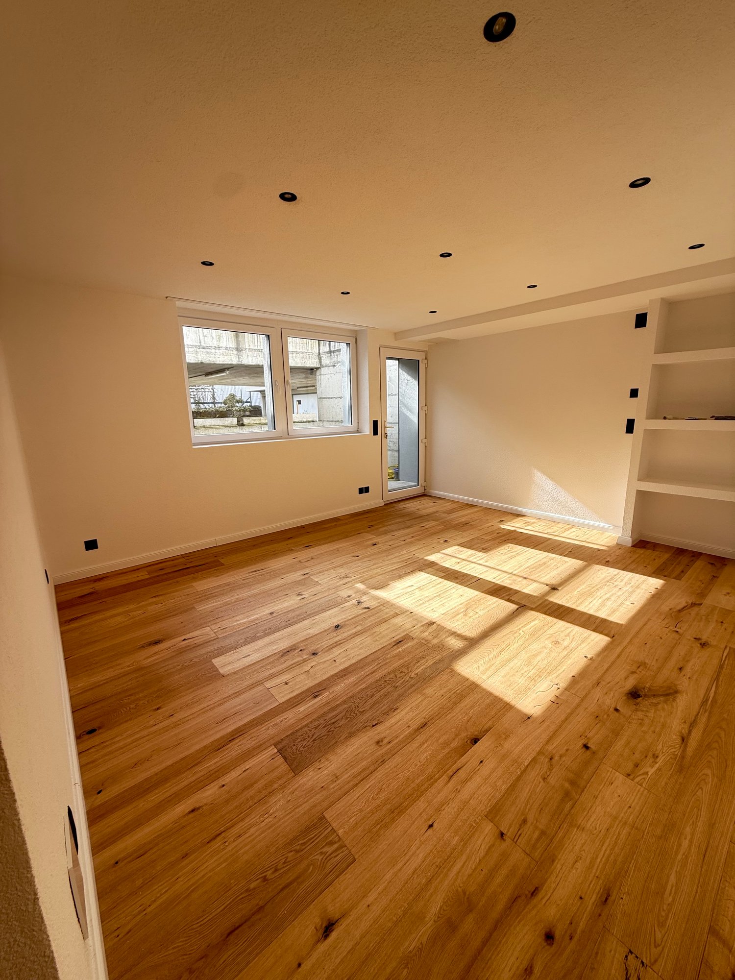 Empty room with hardwood floors, white walls, glass door, and windows.