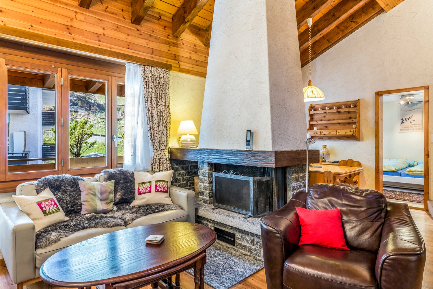 living area with wooden furniture, fireplace, large windows with balcony access, sofa with fur blanket, table, wooden floor