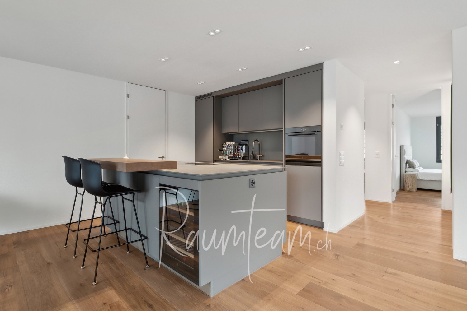 modern kitchen with island, gray cupboards, white walls, black bar stools, wooden floor, coffee machine