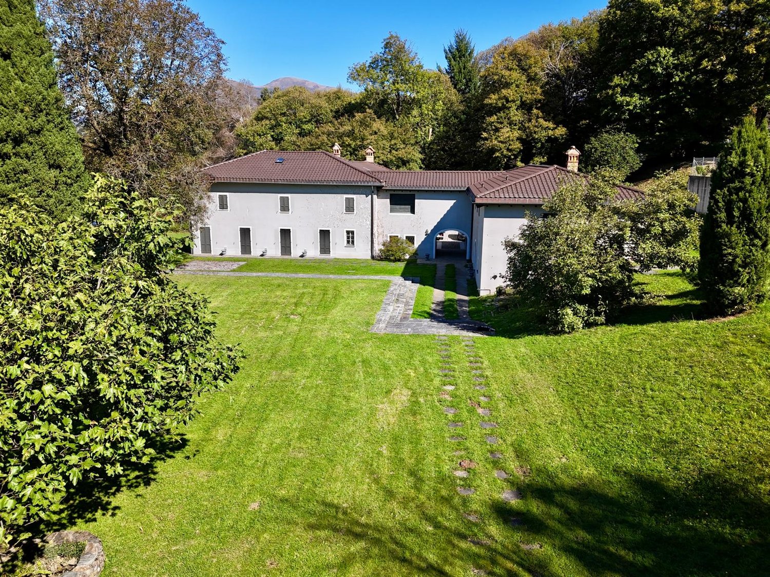 villa with garden, paved driveway, brown roof, surrounded by trees and mountains