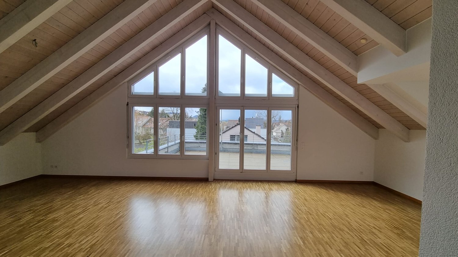 empty attic room, large triangular windows, wooden floor, glass doors to balcony