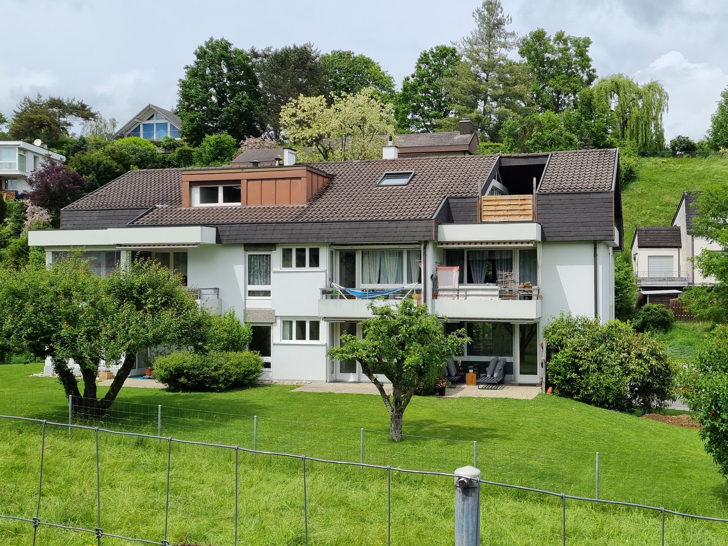 2 story house, white facade, brown roof, balcony on second floor, large garden, seating area