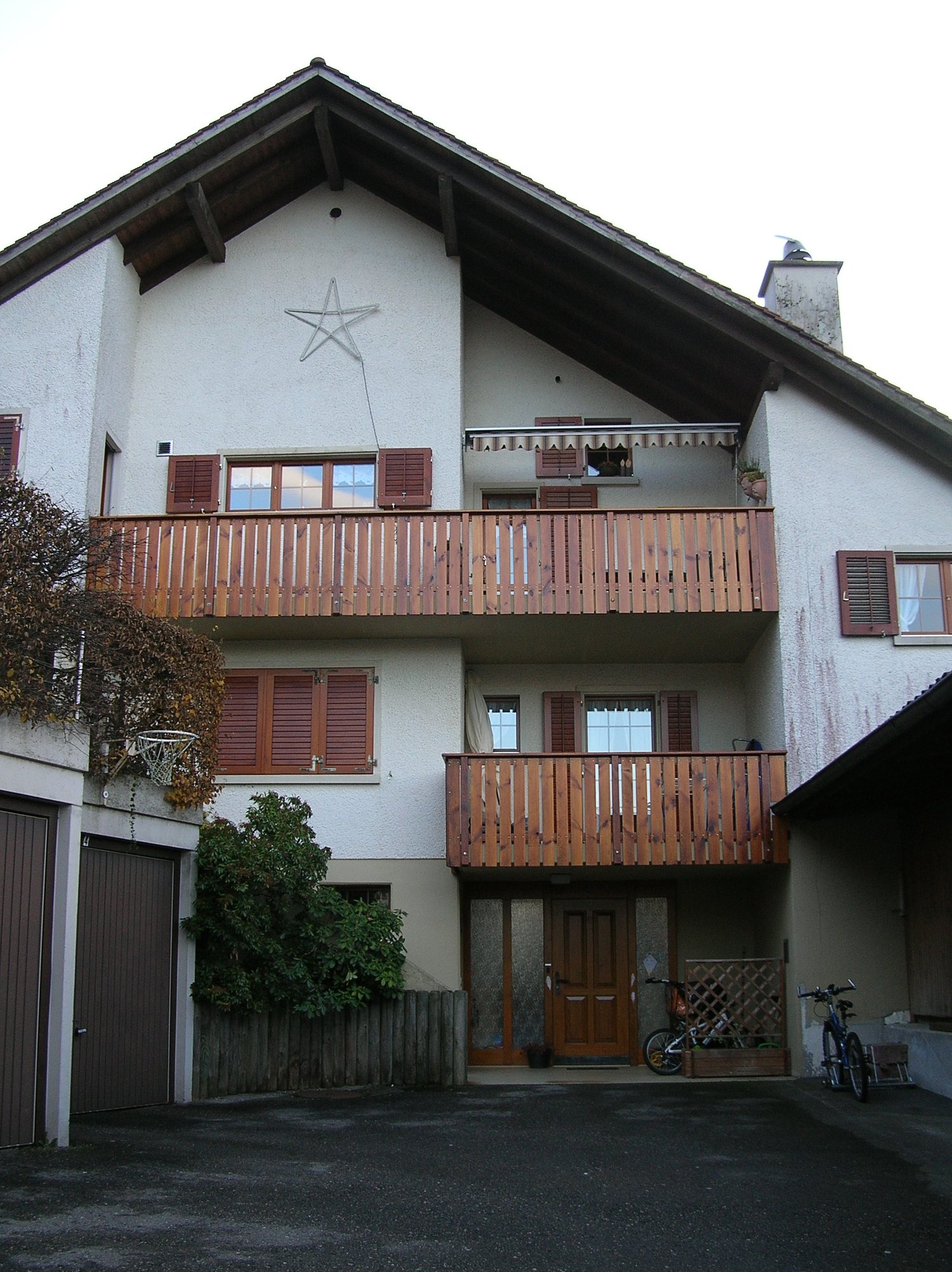 3 story white house, brown roof, 2 balconies, 2 garages, bicycles parked outside