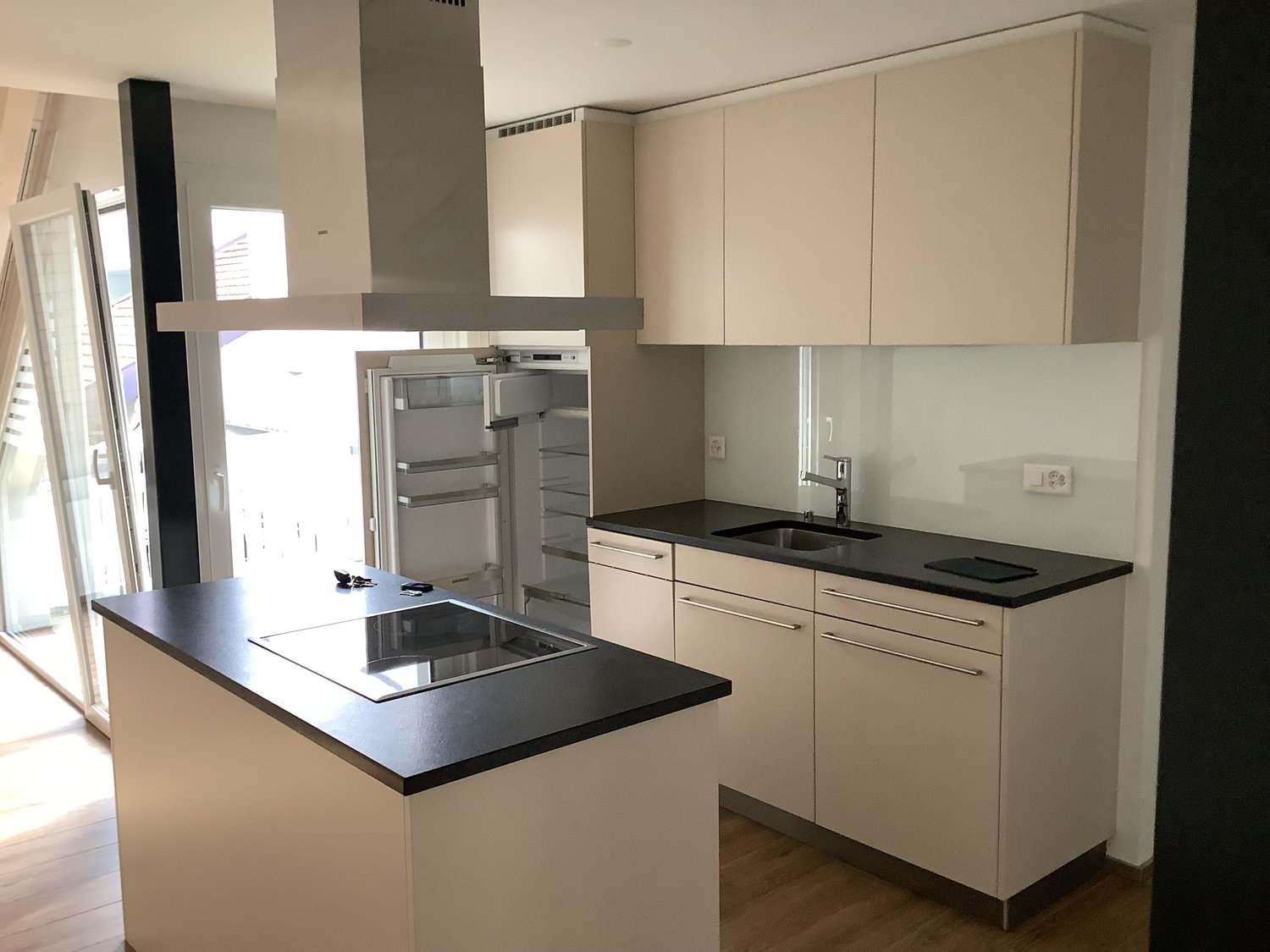 modern kitchen, black countertops, white cabinets, open fridge, glass backsplash, induction stove, stainless steel sink, faucet, open balcony doors