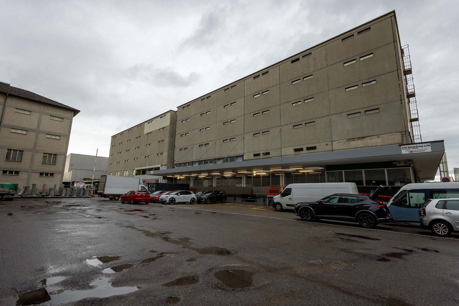 multi-storey building, parking lot, grey exterior, multiple windows, parked cars