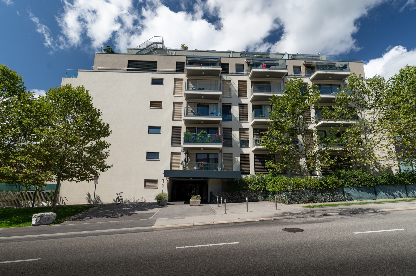 5 story building, beige exterior, balconies, trees, parking area, entrance