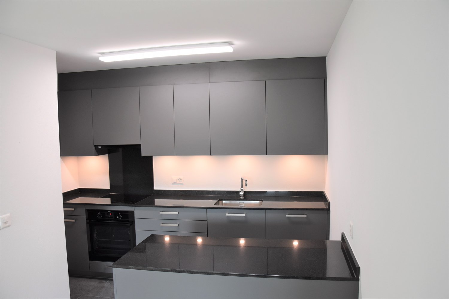 gray cabinets, black countertops, stainless steel sink, modern appliances, built-in oven, dishwasher, washing machine