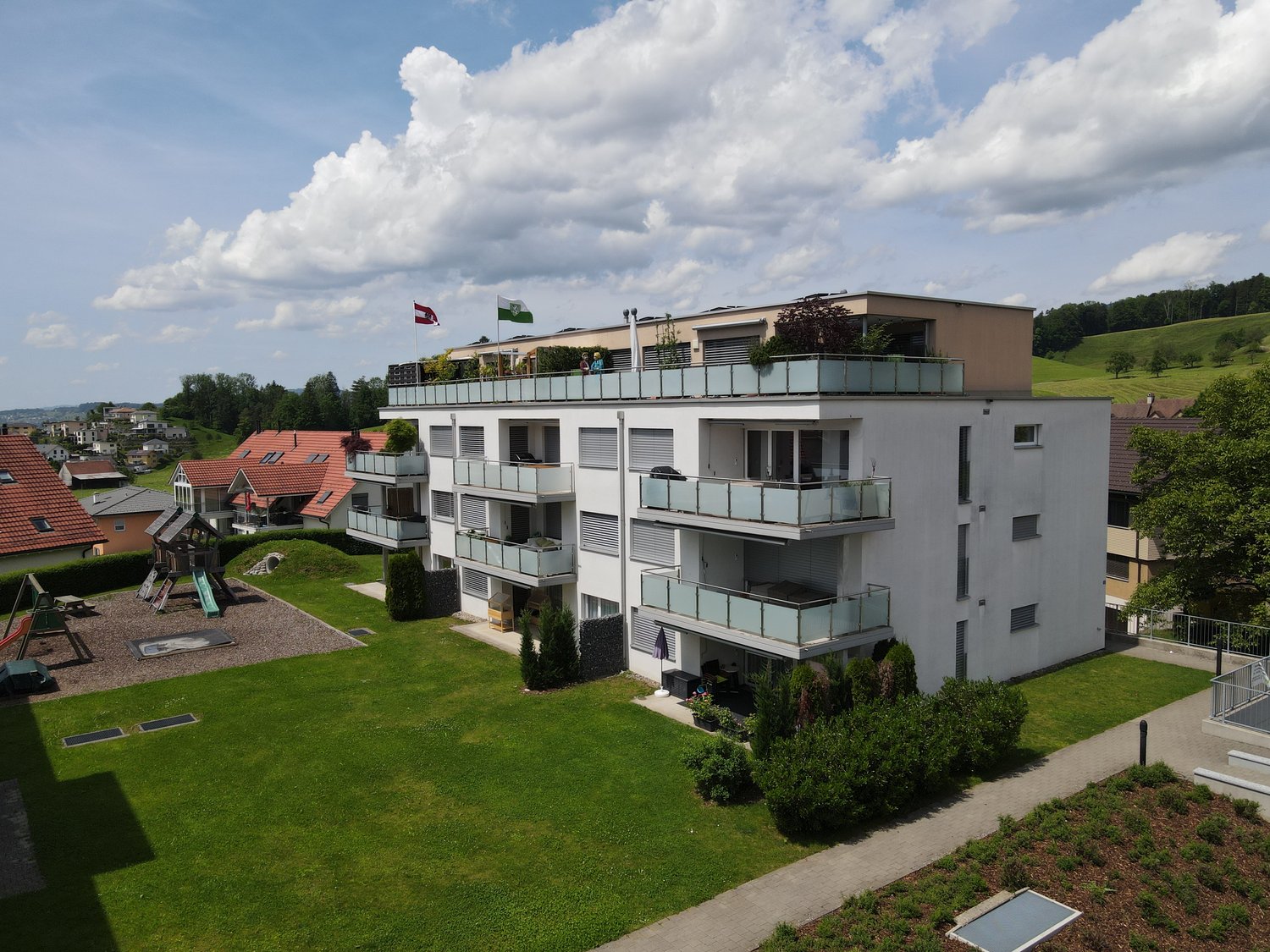 White modern apartment building, 3 story, balconies, green playground